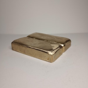 May include: Two gold-colored rectangular bars stacked on top of each other. The bars are smooth and have a slightly rounded edge.