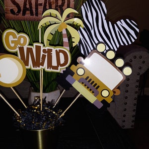 May include: A set of safari-themed party decorations. The decorations include a jeep, a palm tree, a zebra print, and signs that say "Safari" and "Go Wild".