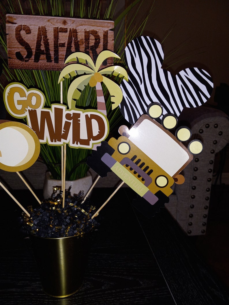 May include: A set of safari-themed party decorations. The decorations include a jeep, a palm tree, a zebra print, and signs that say "Safari" and "Go Wild".