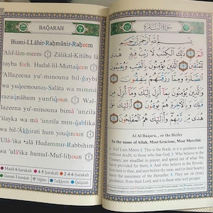 May include: A page from the Quran, the Islamic holy book, in Arabic script. The page features the first verses of the second chapter, Al-Baqarah, which translates to "The Cow". The text is highlighted in different colors and includes the Arabic phrase "Bismillah-ir-Rahman-ir-Rahim", which means "In the name of Allah, the Most Gracious, the Most Merciful".