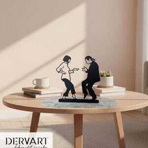 May include: A black metal silhouette sculpture depicting two figures in a dancing pose, mounted on a rectangular base. The design features a person with a bob haircut and a person with long hair tied back, both captured in a mid-motion dance stance.
