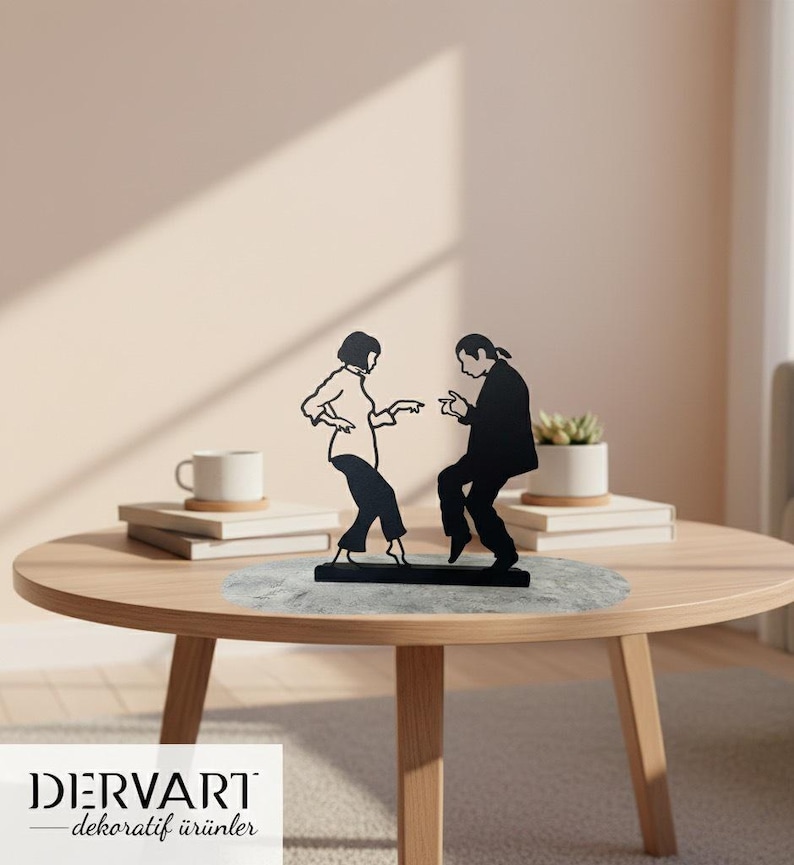 May include: A black metal silhouette sculpture depicting two figures in a dancing pose, mounted on a rectangular base. The design features a person with a bob haircut and a person with long hair tied back, both captured in a mid-motion dance stance.