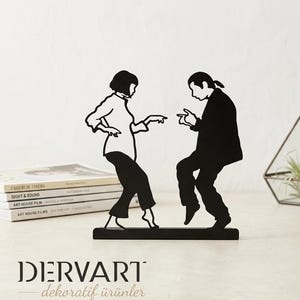 May include: A black metal silhouette sculpture depicting two figures dancing, inspired by a famous film scene. The figures are shown in a dynamic pose, with one person in a shirt and pants and the other in a jacket and trousers, mounted on a rectangular base.