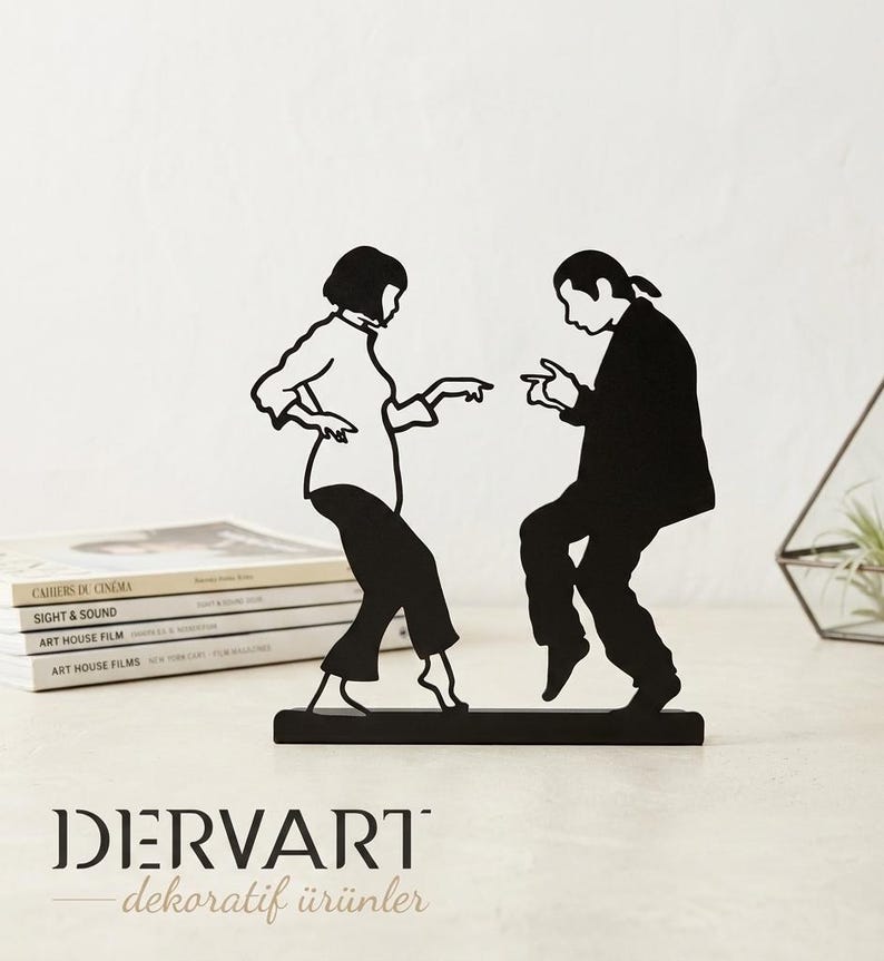 May include: A black metal silhouette sculpture depicting two figures dancing, inspired by a famous film scene. The figures are shown in a dynamic pose, with one person in a shirt and pants and the other in a jacket and trousers, mounted on a rectangular base.