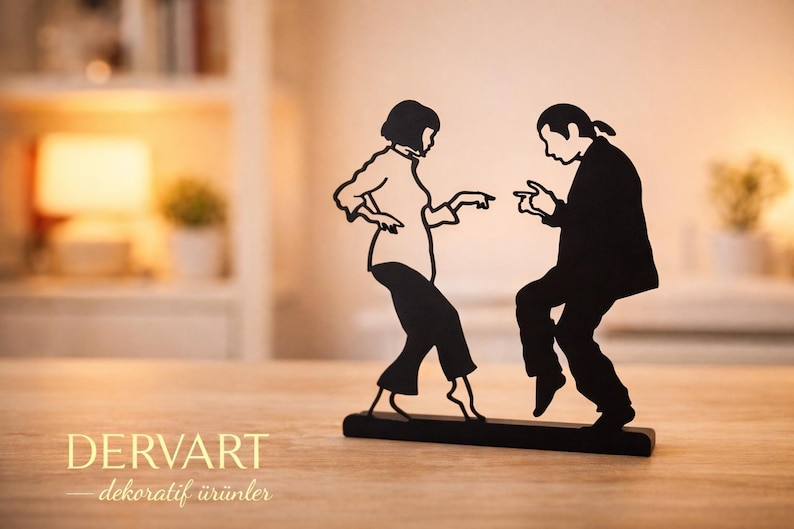 May include: A black metal silhouette sculpture depicting two figures dancing, with one person in a collared shirt and trousers and the other in a jacket and trousers, mounted on a rectangular black base. The text DERVART dekoratif &uuml;r&uuml;nler is visible.