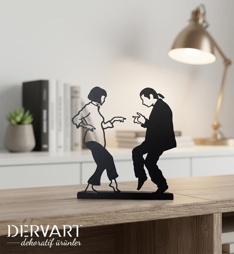 May include: A black metal silhouette sculpture depicting two figures in a dancing pose, featuring a person with a bob haircut and a person with a ponytail, both captured in a mid-motion stance, mounted on a rectangular black metal base.