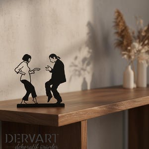 May include: A black metal silhouette sculpture depicting two figures in a dancing pose, inspired by a famous film scene. The figures are shown in profile, with one person wearing a collared shirt and trousers, and the other in a suit jacket.