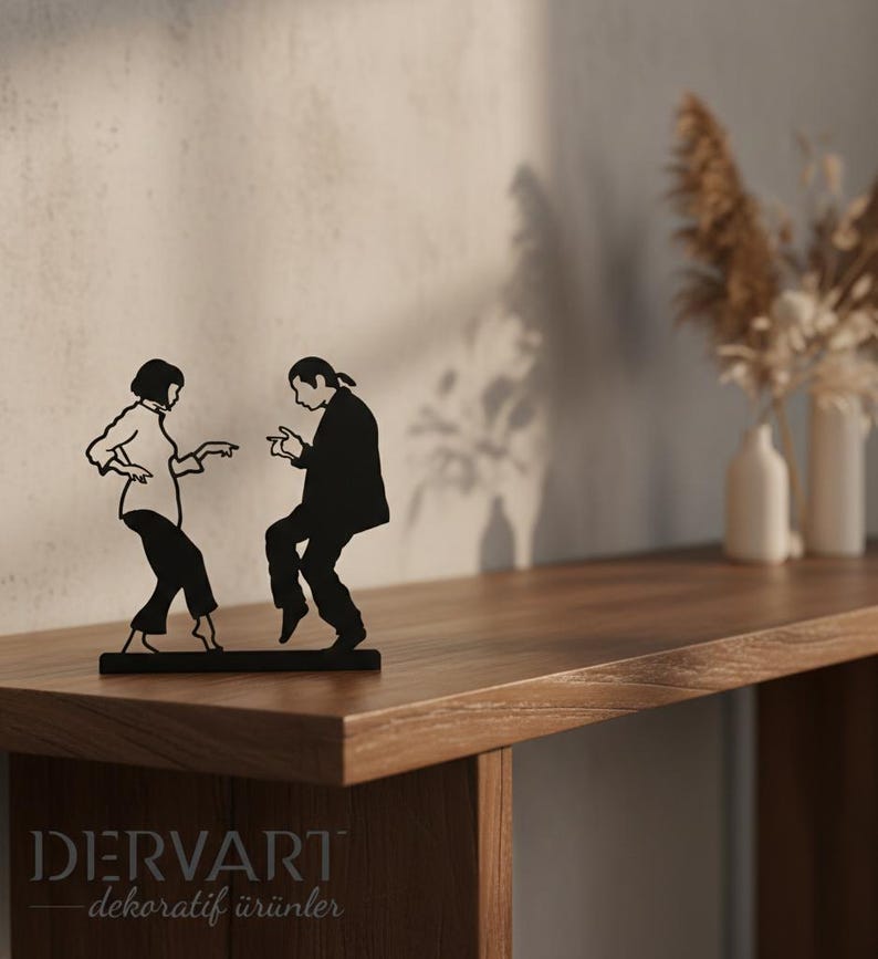 May include: A black metal silhouette sculpture depicting two figures in a dancing pose, inspired by a famous film scene. The figures are shown in profile, with one person wearing a collared shirt and trousers, and the other in a suit jacket.