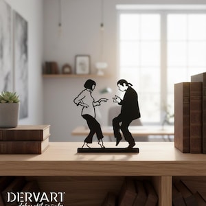 May include: A black metal silhouette sculpture depicting two figures in a dancing pose, mounted on a rectangular base. The design features a person with a bob haircut and a person with long hair tied back, both captured in a mid-dance motion.