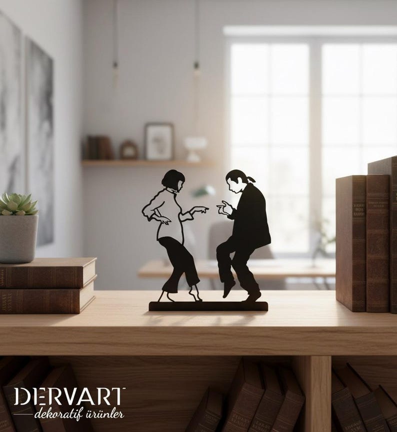 May include: A black metal silhouette sculpture depicting two figures in a dancing pose, mounted on a rectangular base. The design features a person with a bob haircut and a person with long hair tied back, both captured in a mid-dance motion.