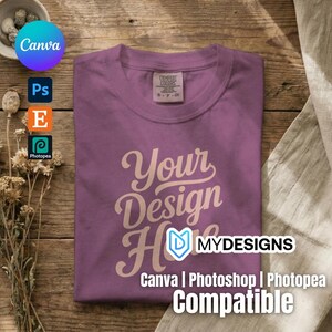 May include: A purple short-sleeved t-shirt with a crew neckline and a Comfort Colors brand label at the inner neck. The shirt features the text Your Design Here in a light-colored script font centered on the front of the garment.