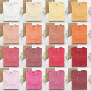 K&ouml;nnte beinhalten: Ein Raster von sechzehn leeren T-Shirts in verschiedenen Farben, darunter Wei&szlig;, Beige, Gelb, Pfirsich, Rosa und Burgunderrot. Jedes Hemd ist ordentlich gefaltet und auf einem neutralen Hintergrund pr&auml;sentiert, um die verschiedenen Farboptionen zu zeigen.