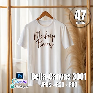 Puede incluir: Maqueta de camiseta blanca con el texto "Mockup Berry" en letras marrones. La camiseta está colgada de una percha de madera sobre un fondo blanco. El texto "Bella+Canvas 3001 JPGS + PSD + PNG" está en la parte inferior de la imagen.