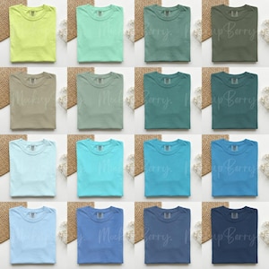K&ouml;nnte beinhalten: Eine Sammlung gefalteter T-Shirts in verschiedenen Farben, darunter Gr&uuml;n, Blau und Beige. Die Hemden sind in Reihen und Spalten angeordnet und zeigen eine Reihe von Farbt&ouml;nen. Jedes Hemd hat eine einfarbige Farbe und bietet eine klare und einfache &Auml;sthetik.
