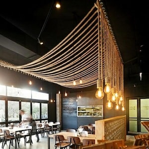Peut inclure: Intérieur d'un restaurant avec un éclairage original. De grosses cordes sont suspendues au plafond en forme de vagues, avec des ampoules suspendues. L'espace a des murs sombres, des tables et des chaises, créant une atmosphère chaleureuse.