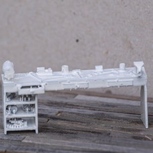 May include: A white 3D printed model of a workbench with a shelf on the left side. The workbench has a variety of tools and equipment on the top surface.