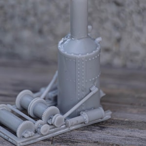 Op de afbeelding: Een grijs plastic model van een stoomgevoede lier met een grote cilindrische ketel en meerdere tandwielen. De lier is gemonteerd op een basis met een reeks wielen.