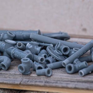 Puede incluir: Un montón de accesorios y conectores de tubería de plástico gris. Los accesorios son de varios tamaños y formas, incluyendo codos, tees y conectores rectos.