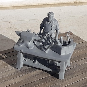 Pode incluir: Figura cinzenta de um ferreiro em miniatura com uma bigorna, ferramentas e uma figura de um ferreiro a trabalhar. A figura está numa superfície de madeira.