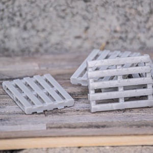 Op de afbeelding: Drie grijze miniatuurhouten pallets, op elkaar gestapeld, op een houten oppervlak.