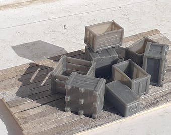 May include: A collection of small, gray miniature crates of various designs. Some have slatted sides, while others are solid. The crates are arranged on a wooden surface, suggesting a rustic or industrial theme.