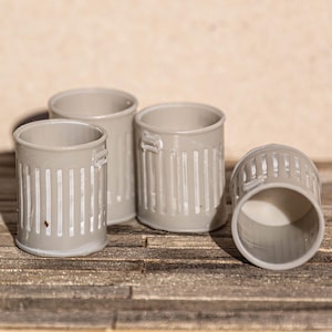 Puede incluir: Cuatro pequeños cubos de basura de metal gris con textura acanalada. Los cubos están dispuestos en fila sobre una superficie de madera.