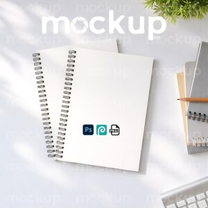 May include: White spiral-bound notebooks with a black metal binding. The notebooks are on a white surface, with the word "mockup" in white text. Icons for Ps, a teal swirl, and PNG are visible. A pencil and keyboard are also in the image.