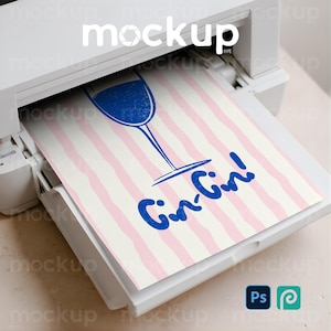 Könnte beinhalten: Ein weißer Drucker druckt ein Blatt Papier mit rosa und weißen Streifen. Das Papier hat eine blaue Illustration eines Weinglases und die Worte "Gin-Gin!" in Blau. Enthält Photoshop- und Procreate-Logos.