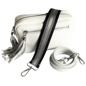 May include: White leather crossbody bag with a black and silver striped strap and a white tassel. The bag has a zip closure and a small pocket on the front.