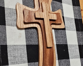 May include: A wooden cross with a layered design, featuring three different shades of brown wood. The cross is displayed against a black and white checkered background.