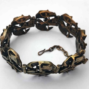 May include: A gold-toned bracelet with a unique, intricate design. The bracelet is made of multiple linked pieces, each with a different pattern. The bracelet has a clasp closure.