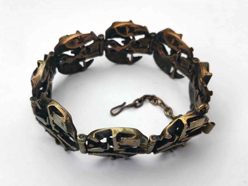 May include: A gold-toned bracelet with a unique, intricate design. The bracelet is made of multiple linked pieces, each with a different pattern. The bracelet has a clasp closure.