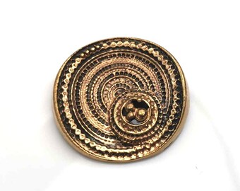 May include: A round, gold-toned metal button with a concentric circle design and a smaller circle in the center with three raised dots.