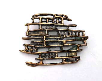 May include: A gold-toned abstract brooch with a geometric design. The brooch is made of metal and has a textured surface.
