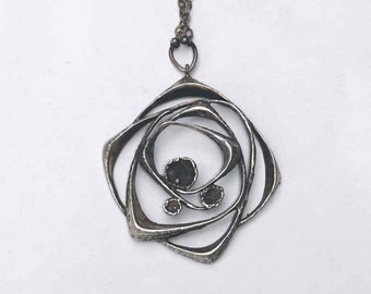 May include: A silver pendant necklace with a geometric design featuring multiple overlapping circles. The pendant has a textured surface and three small, dark gray stones.
