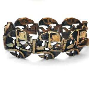 May include: A vintage brass bracelet with a geometric design. The bracelet is made of interlocking circular links with a textured surface.