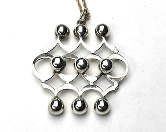 Puede incluir: Un collar con un colgante de plata con un diseño geométrico que presenta una serie de círculos y esferas interconectados.