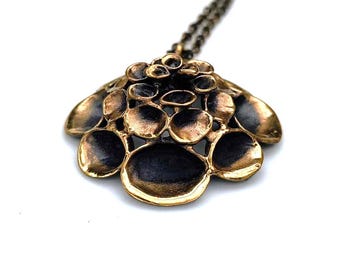 May include: A gold-toned pendant necklace with a large, abstract, flower-shaped design. The pendant is made of multiple overlapping circles, creating a textured and organic look.
