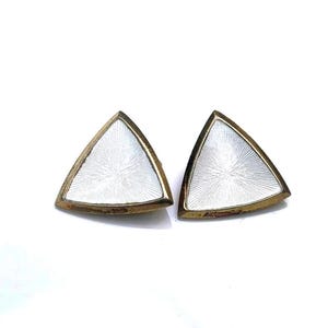 Peut inclure: Une paire de boucles d'oreilles triangulaires en or avec émail blanc. Les boucles d'oreilles ont une surface texturée.