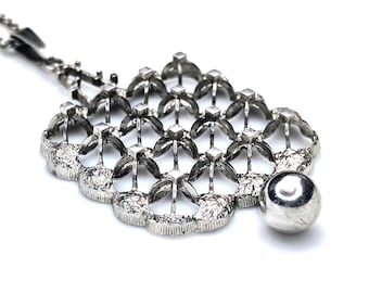 Puede incluir: Un collar de plata con un colgante de diseño geométrico y una cuenta redonda en la parte inferior.
