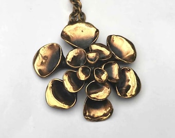 May include: A vintage brass-toned pendant necklace. The pendant features an abstract floral design with multiple rounded, petal-like shapes. The necklace has a matching brass chain.