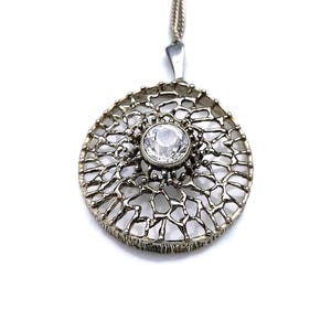 May include: A silver pendant necklace with a round, openwork design featuring a clear crystal in the centre.