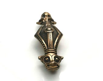 May include: Bronze-colored pendant with an intricate design. The pendant features a detailed, symmetrical pattern with a central shield-like shape and a stylized animal head at the bottom. The overall design suggests a historical or fantasy theme.