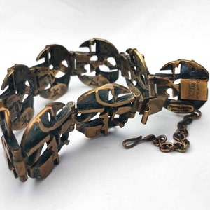May include: A brass bracelet with a unique design featuring interlocking circles and a chain closure. The bracelet is marked "DRIVE THAILAND" on the clasp.