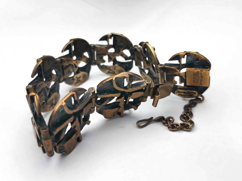 May include: A brass bracelet with a unique design featuring interlocking circles and a chain closure. The bracelet is marked "DRIVE THAILAND" on the clasp.