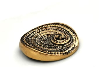 May include: A gold-toned metal pendant with a circular design featuring concentric circles and a smaller, raised circle in the center.