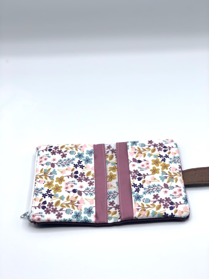 May include: A small floral print wallet with a zipper closure and a brown leather strap. The wallet has a pink and white floral pattern with green leaves.