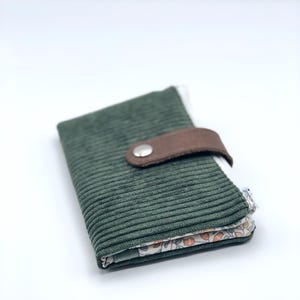 May include: A green corduroy wallet with a brown leather flap and a silver button closure. The wallet has a floral print lining.