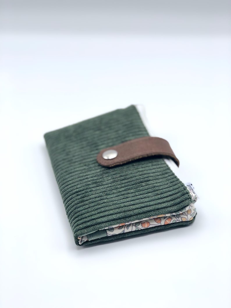 May include: A green corduroy wallet with a brown leather flap and a silver button closure. The wallet has a floral print lining.