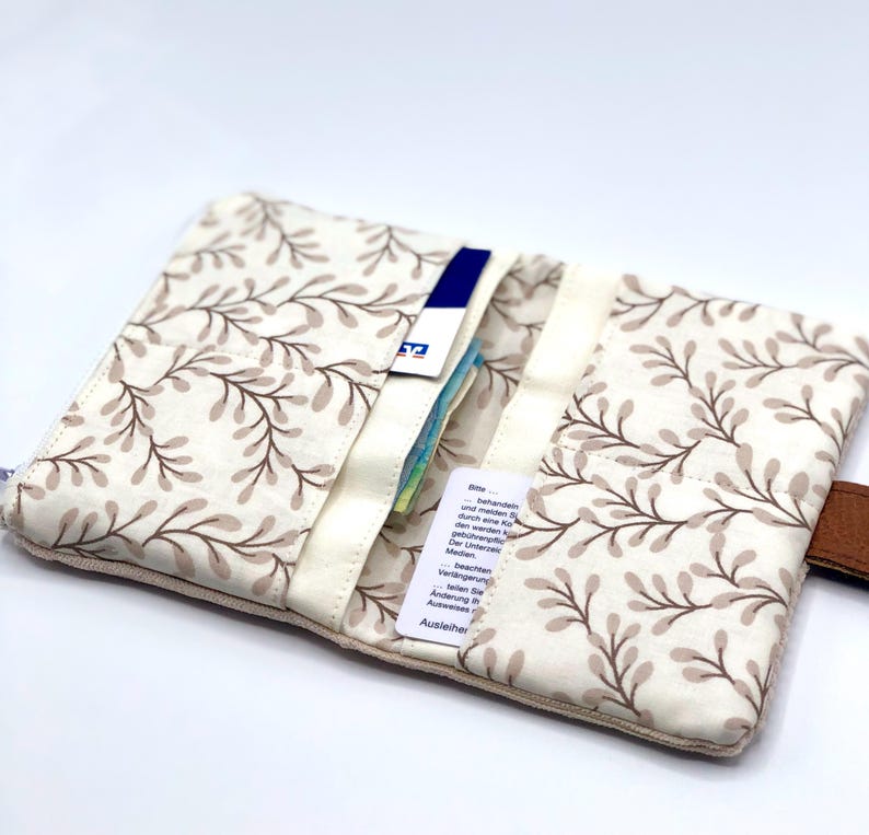 May include: A beige fabric wallet with a brown floral pattern. The wallet has multiple slots for cards and cash. The wallet is open and there are cards and cash inside.